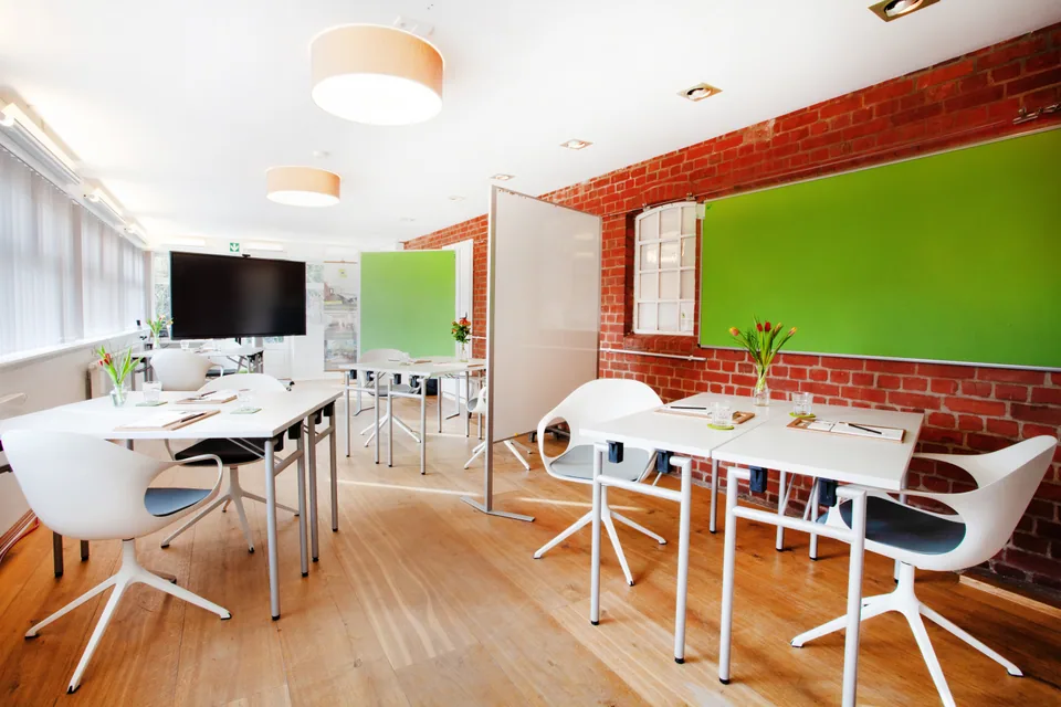 Several group tables, mobile pinboards and a display in the bright Main Meeting Room with a brick wall.