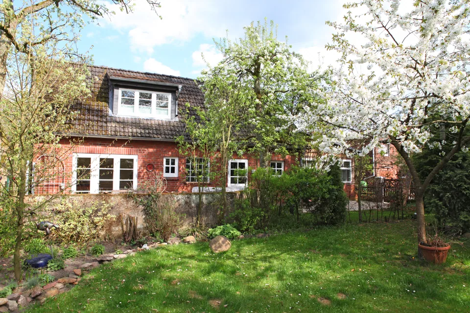 A view of the timber-framed building from the garden, between trees and shrubs.