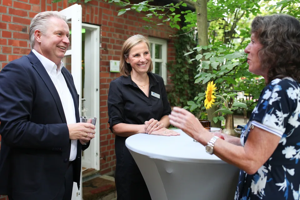 Three guests talking around a high table outdoors.