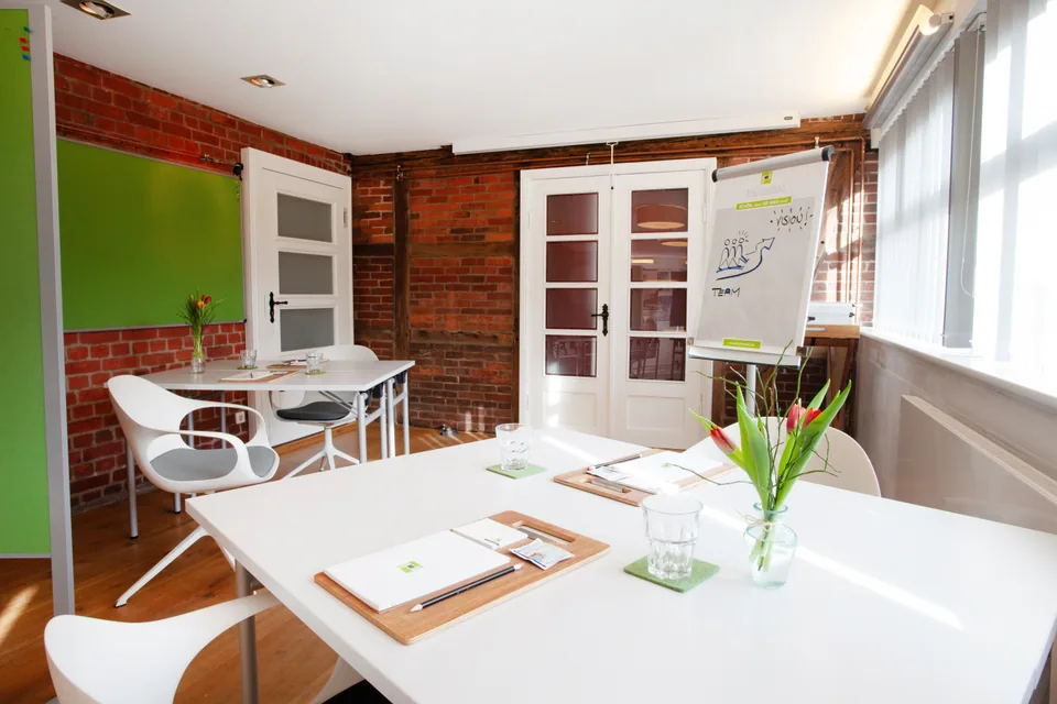 Prepared tables with notepads, green pinboards and a flipchart in the bright Main Meeting Room.