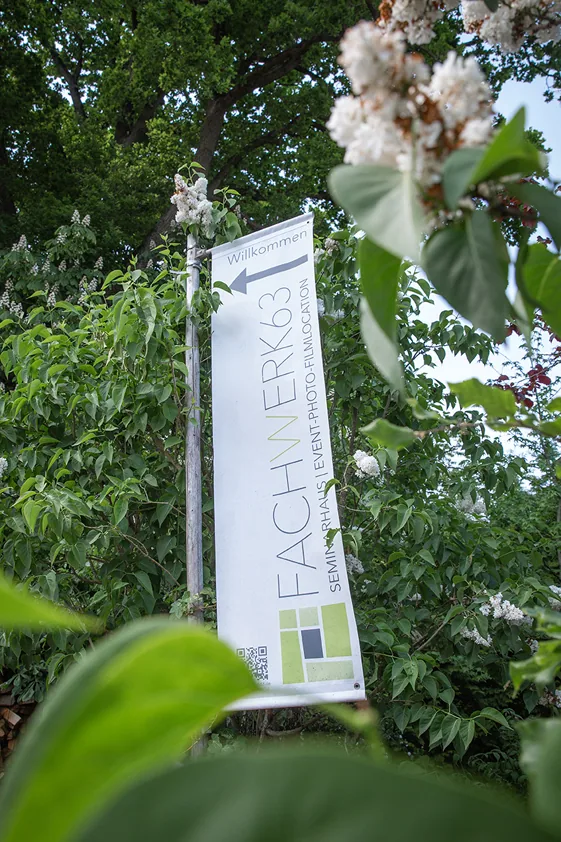 A Fachwerk63 welcome sign with a direction arrow among green leaves.